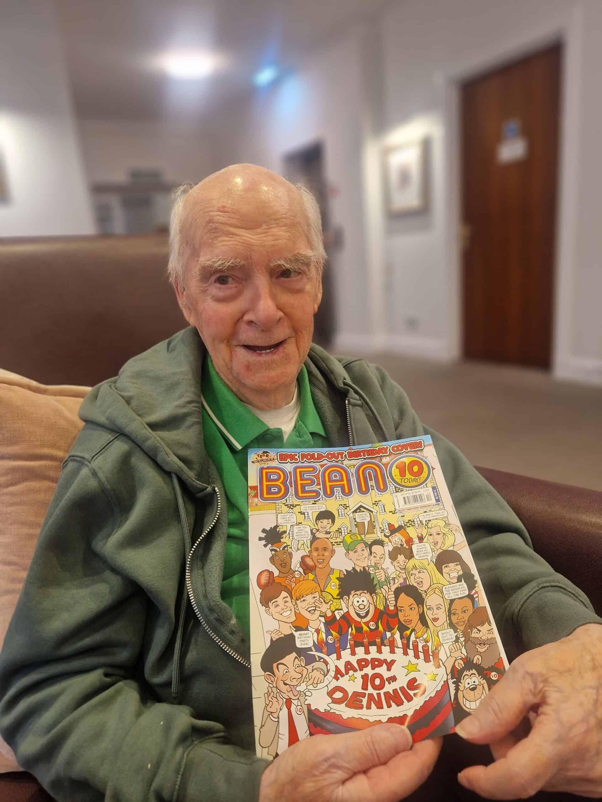 Elderly man holding a Dennis the Menace comic book in a care home.