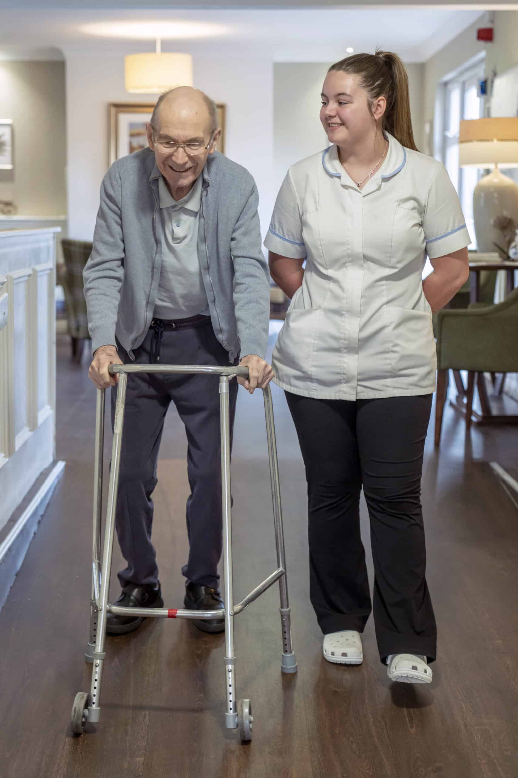Elderly man using a walker with a caregiver providing support and companionship.