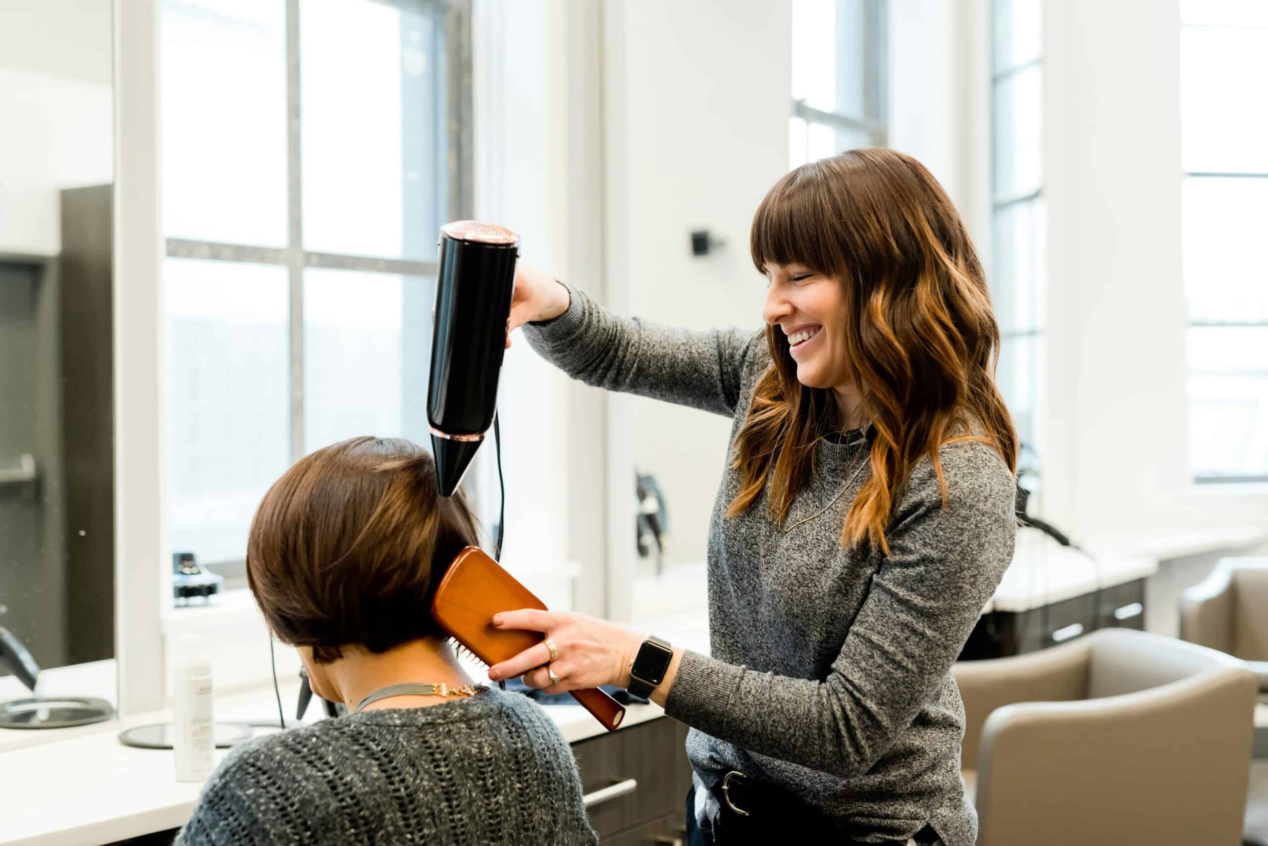 Professional hairdresser blow-drying a client's short hairstyle in a modern salon.