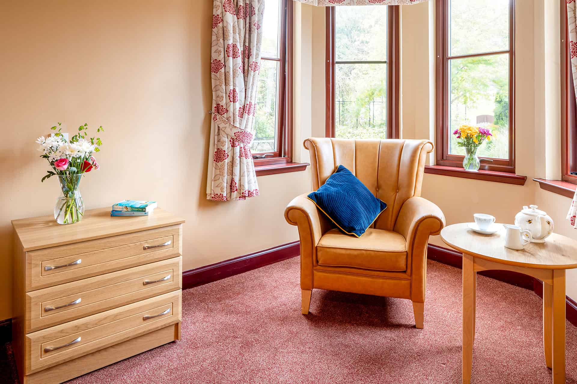 Comfortable armchair by windows with floral curtains and side table.